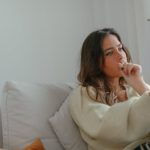 A woman sitting on a couch indoors, thoughtfully reading a book in a cozy setting.